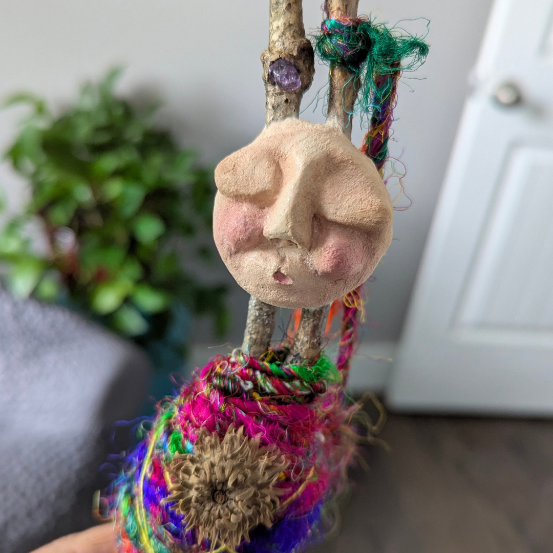 Handmade clay face attached to a colorful fiber-wrapped Bundle Doll.