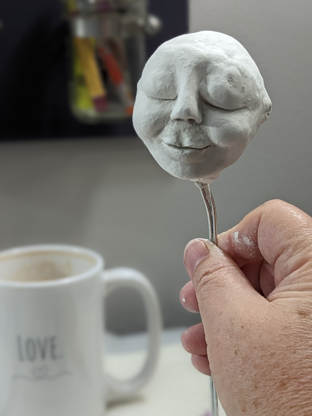 Close-up of a hand holding a clay spirit doll face in progress on a wire armature, created during a private creative retreat in Stacy Vajta’s West Asheville studio.