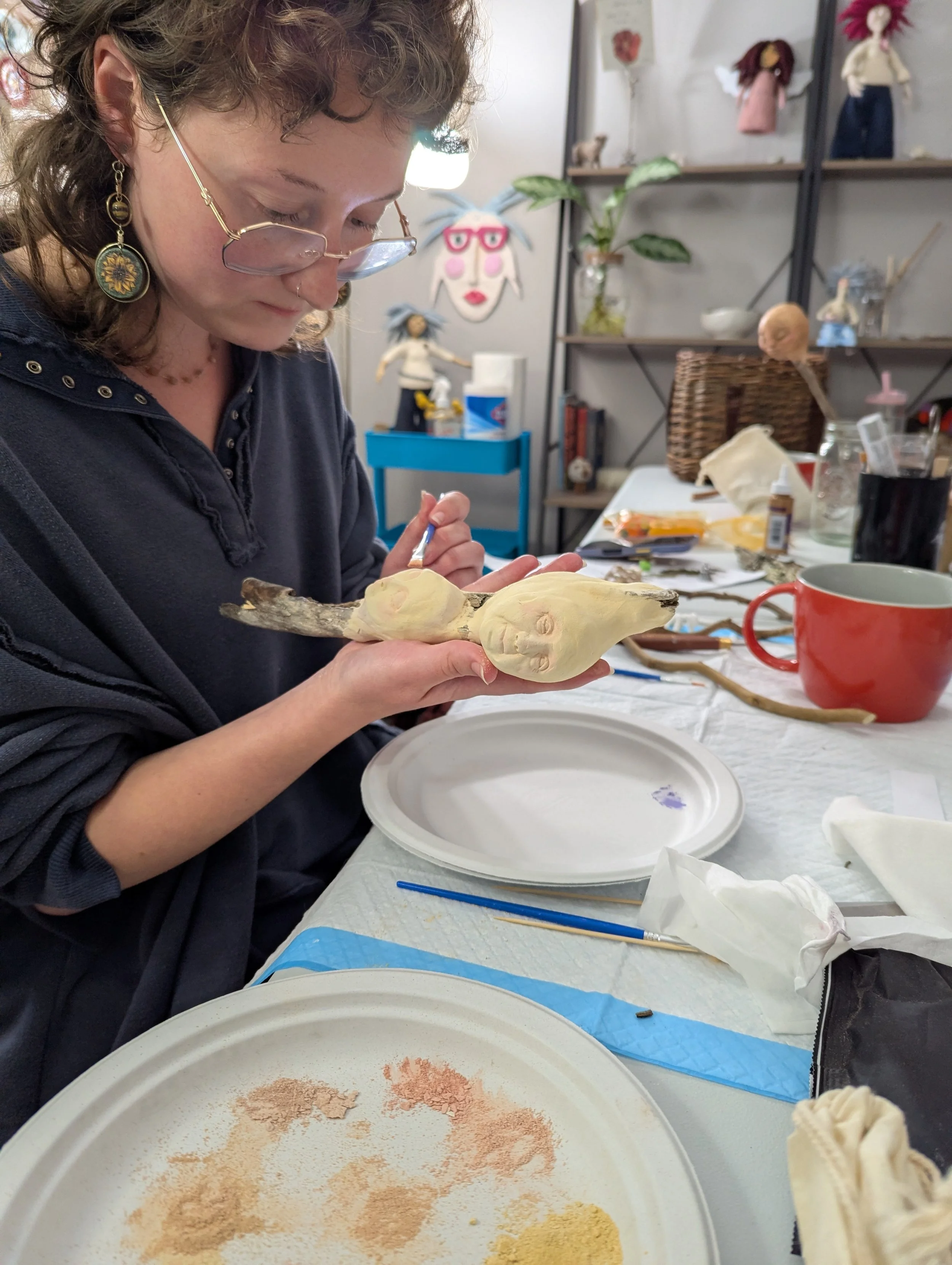 A woman painting clay faces that are part of her stick doll during a creative retreat in Asheville