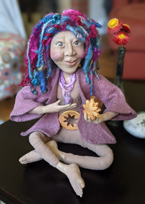 Colorful handmade spirit doll with yarn hair and expressive face sitting with small symbolic objects