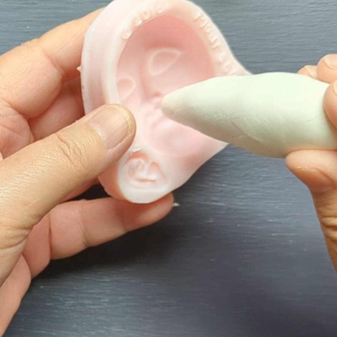 Pressing clay into a silicone face mold to create a simple molded face for a stick doll.