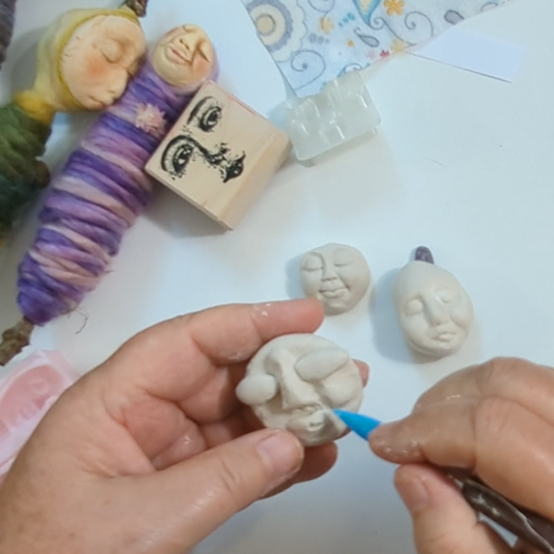 Sculpting details into a small handmade clay face with a modeling tool.