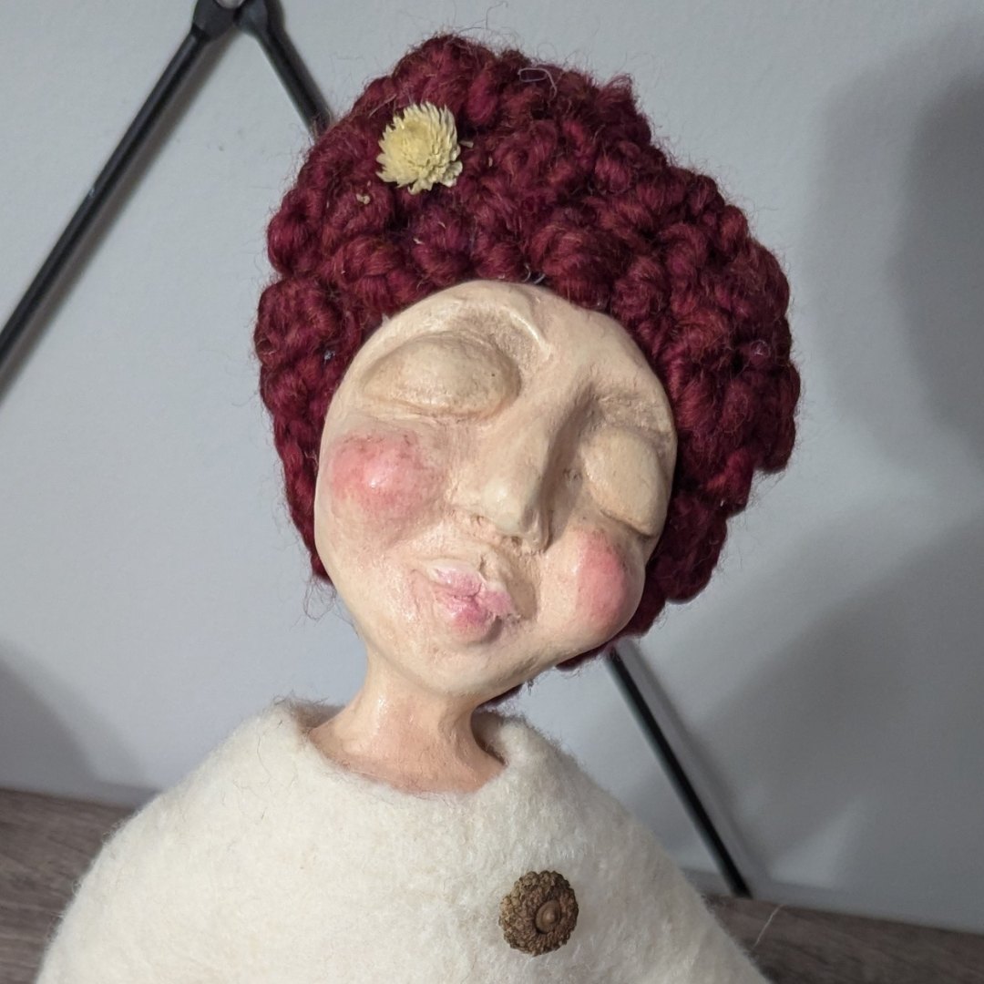 Finished spirit doll with a hand-sculpted clay face, closed eyes, rosy cheeks, and a deep red fiber hair.
