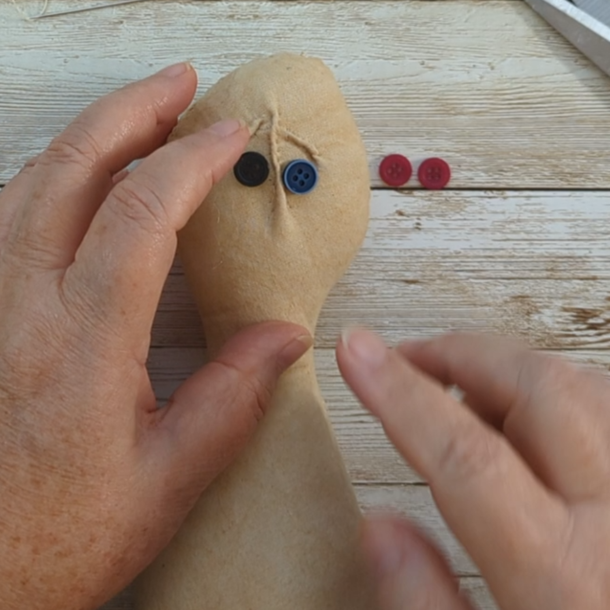 Close-up of hands placing mismatched button eyes on a soft fabric worry doll head during the workshop.