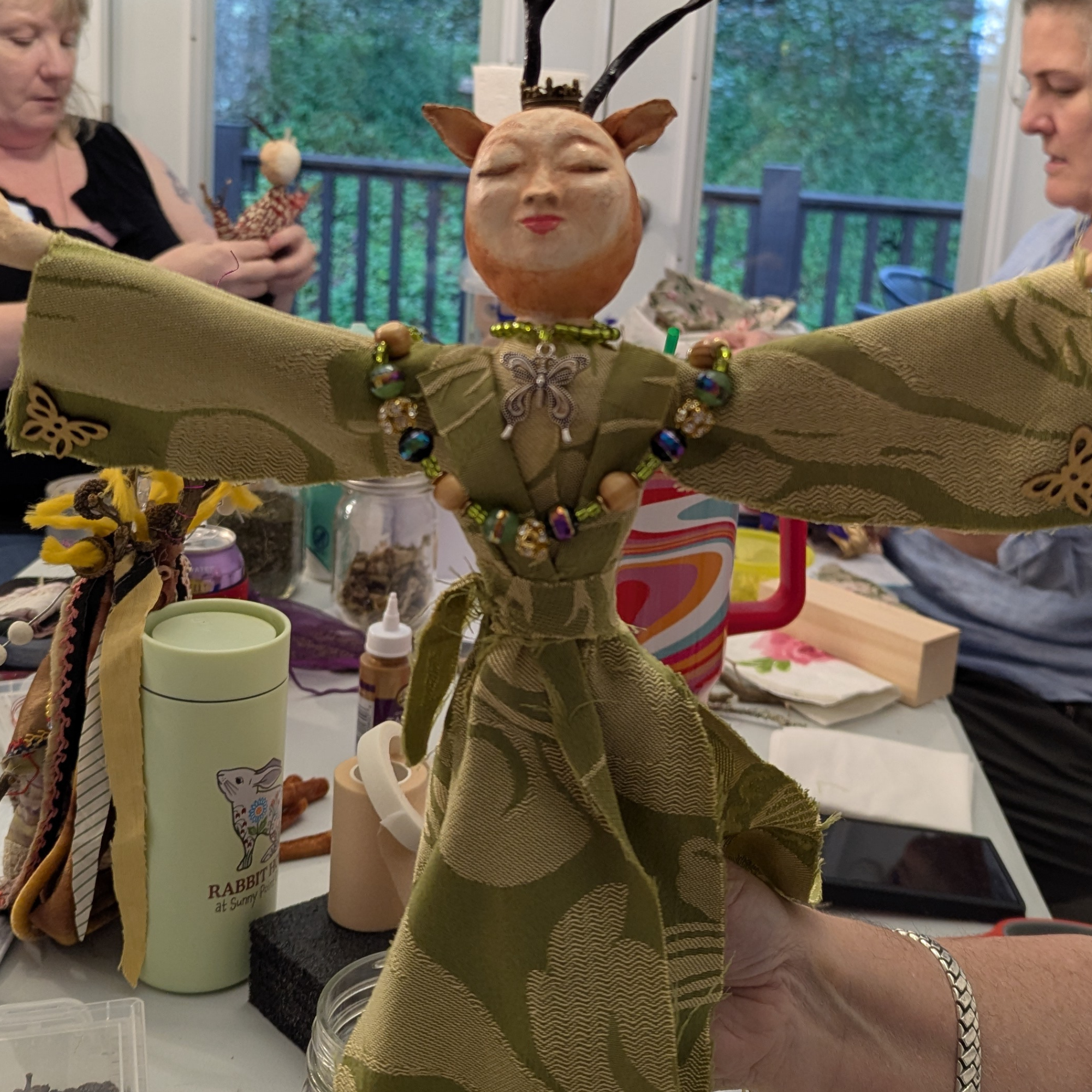 Handmade spirit doll with outstretched arms and decorative details, held during a live workshop.