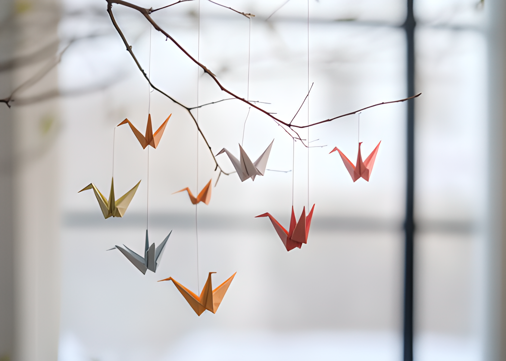 Origami crane intention mobile hanging from a natural branch, with folded paper cranes gently suspended in a light-filled space.