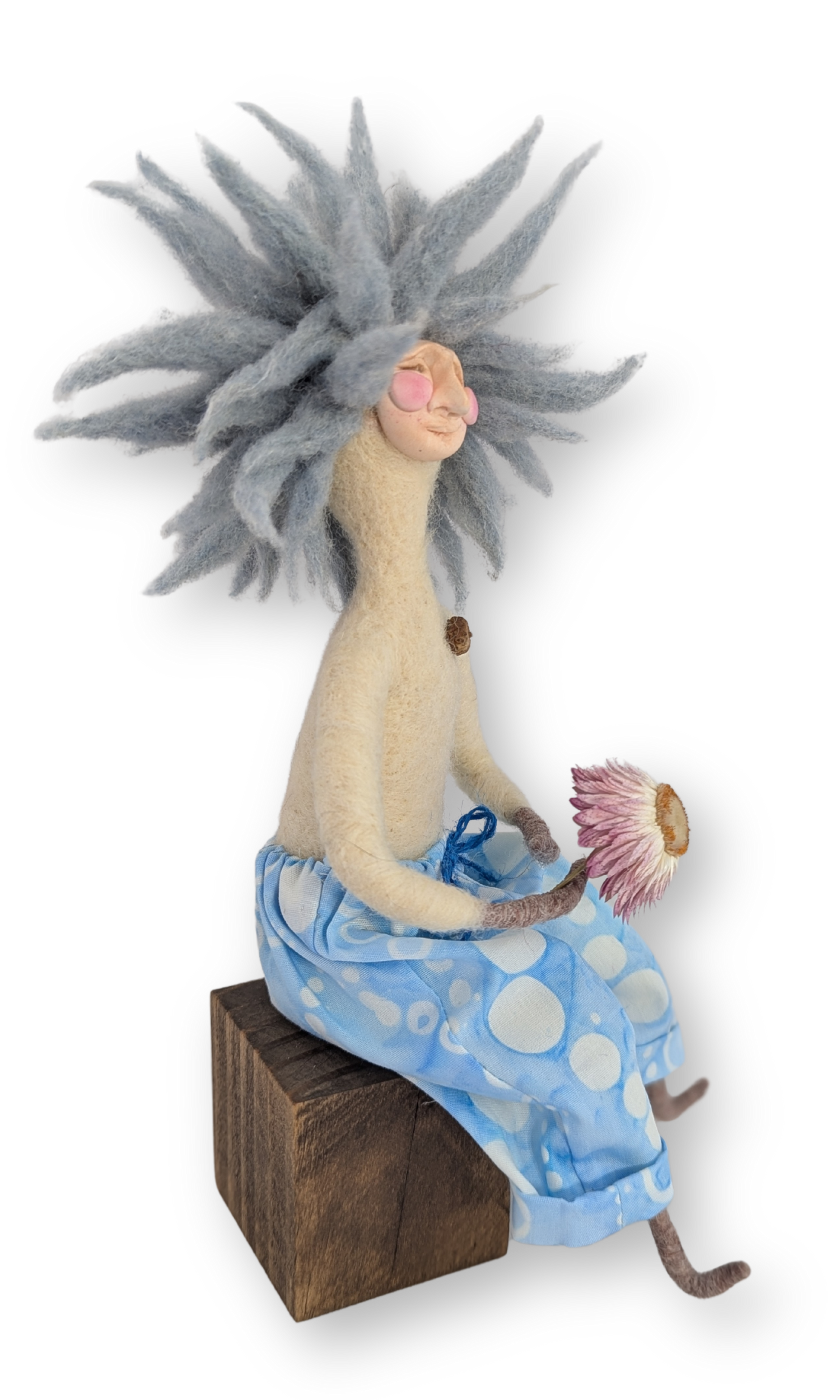 Side view of Surfer Dude Guardian Doll seated on a wood block, holding a dried flower in relaxed pose.