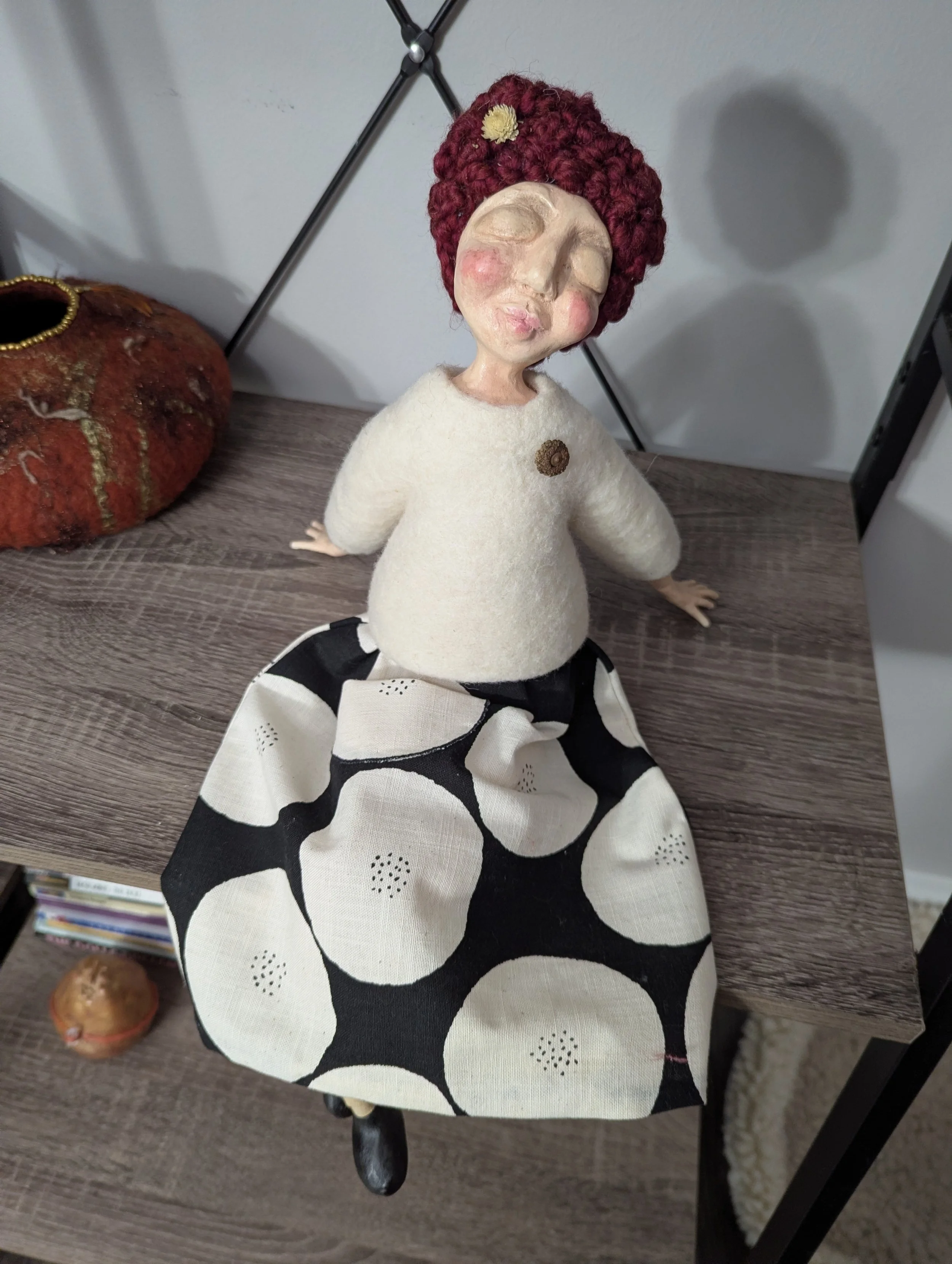 Handmade spirit doll sample for an online workshop, with a clay face, red yarn hair, cream fabric body, black and white skirt, and small symbolic details.
