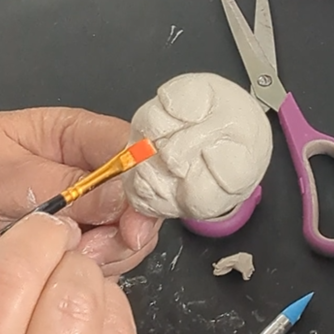 Smoothing and blending features on a handmade clay face with a small brush.