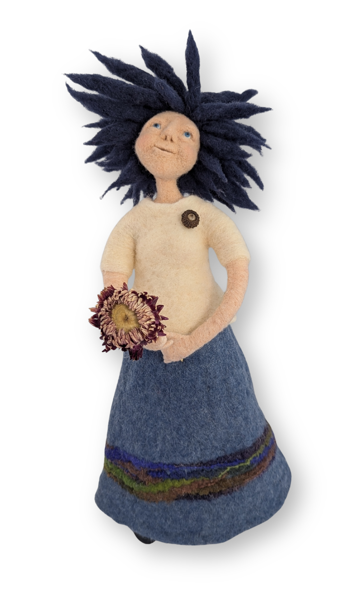 Dreamer Guardian Doll standing, holding a dried flower, with navy hair and a felted blue skirt with embroidered details.