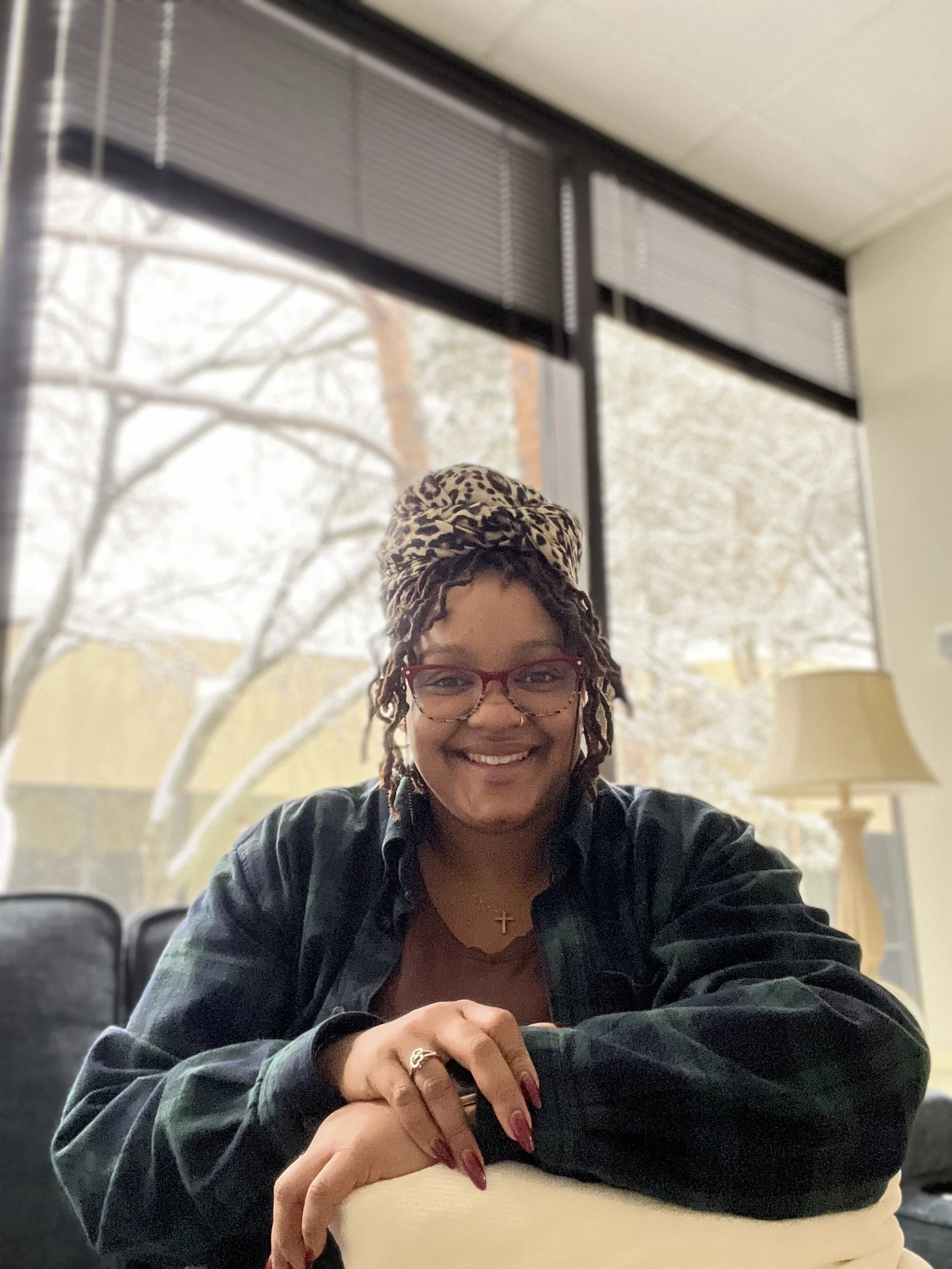 Avery Poole, Winger Clinical Counseling DBT and CBT therapist, smiling warmly outdoors in front of a red brick wall with artistic details.


