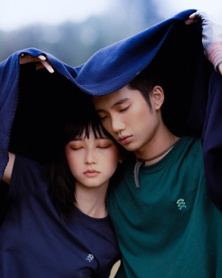 A young woman and a young man with eyes closed, sharing a moment under a blue blanket or towel.