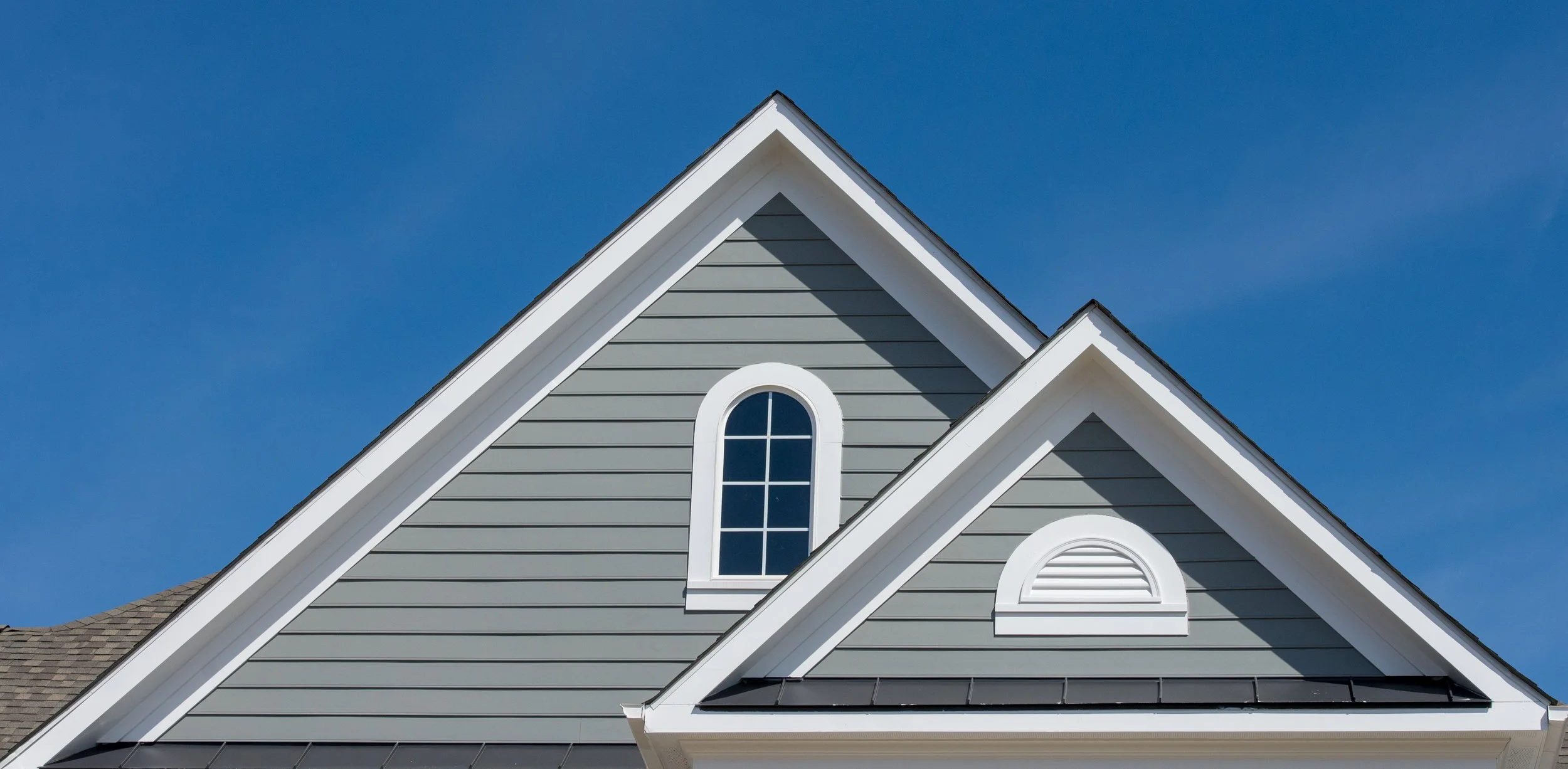 Two gable roofs with gray siding against a clear blue sky.
