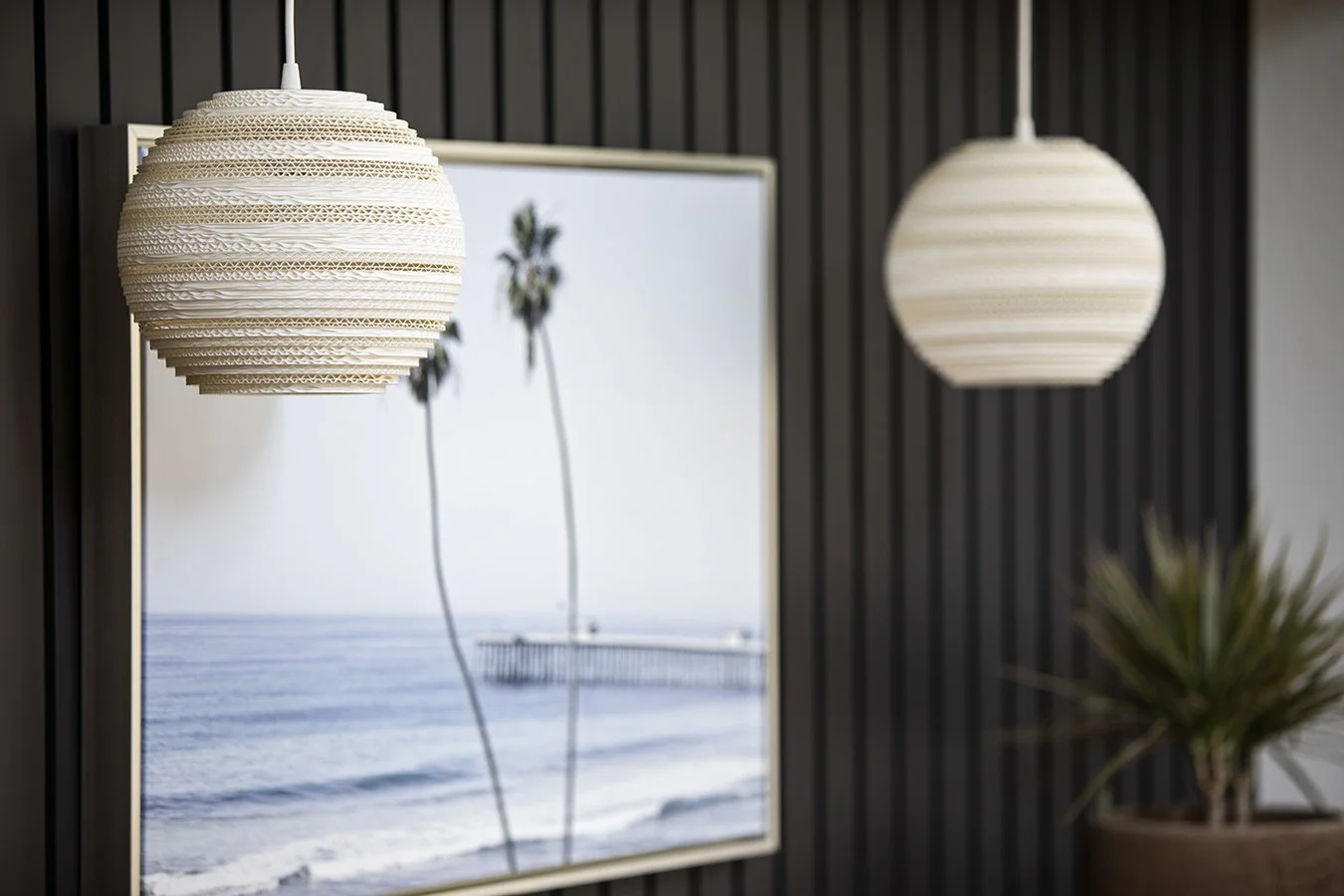 Two hanging pendant lights with a beach scene mirror behind them, showing palm trees and the ocean.
