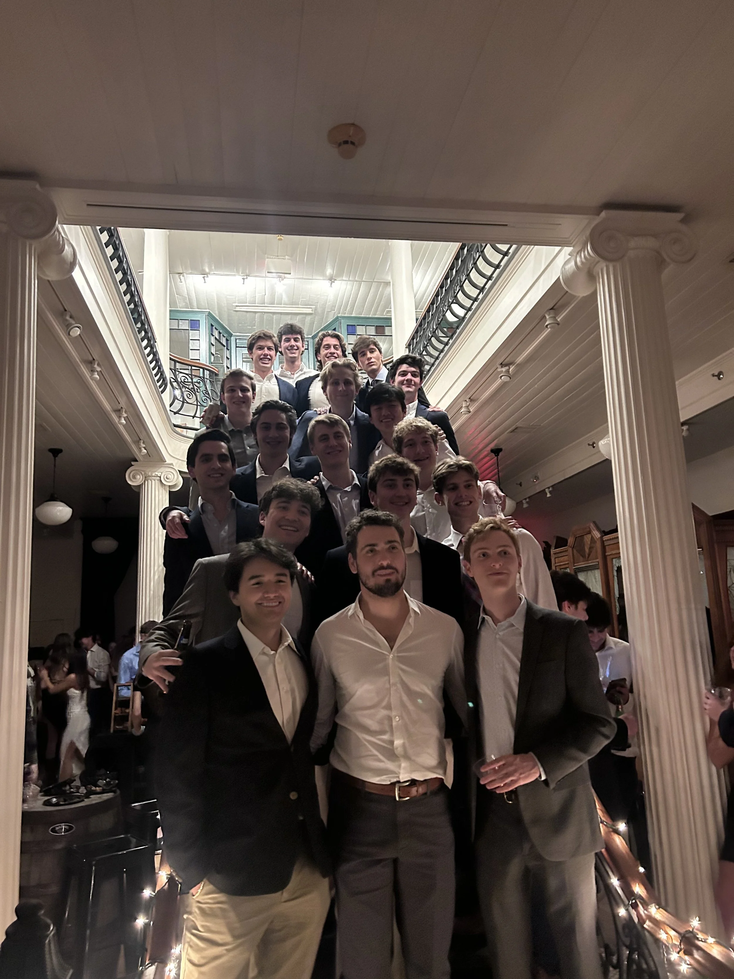 Group of young men in formal attire standing on a staircase in a dimly lit venue