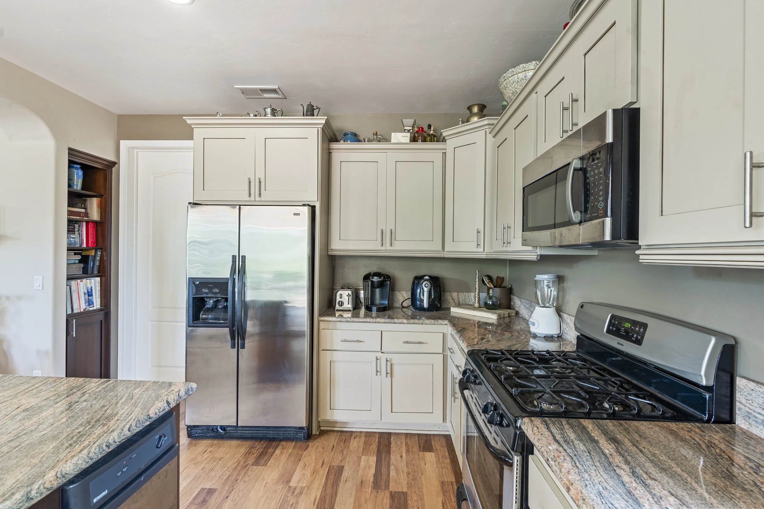 Kitchen with stainless steel refrigerator, microwave, gas stove, white cabinets, granite countertops, and various small appliances on counter.