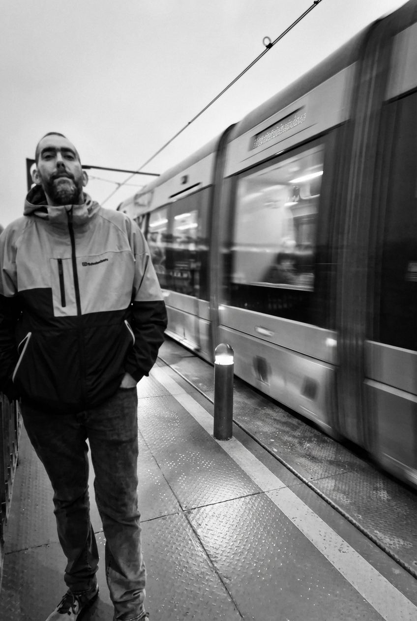 A man standing on a train platform next to a moving train in black and white.