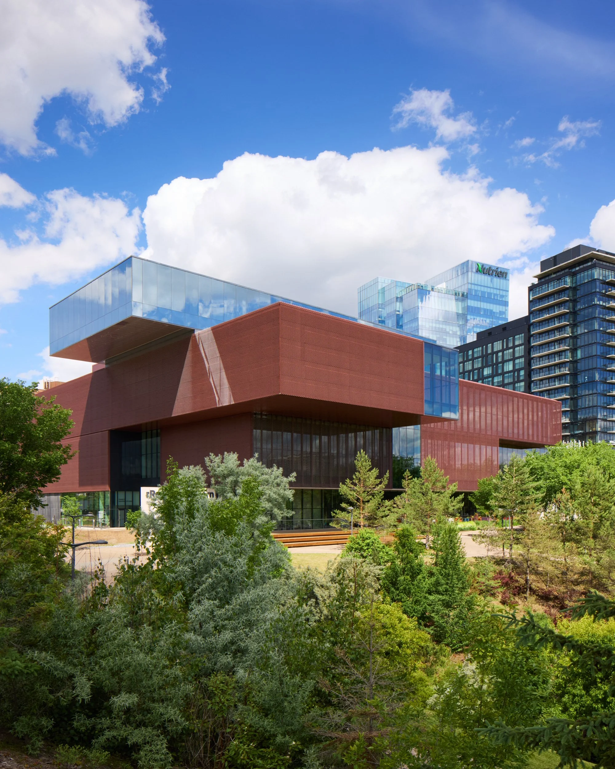 South facade of the Remai Modern Art Gallery in Saskatoon, Saskatchewan. View from across the river. Gallery perched on riverbank above the park. River and walking path in foreground.