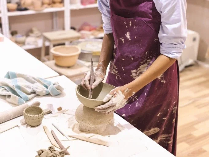 Person crafting a clay bowl on a table with pottery tools.