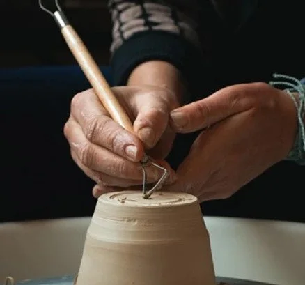 Person shaping clay pottery with a carving tool