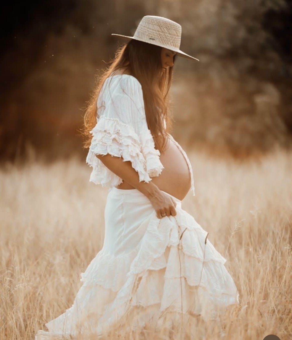 Pregnant woman in white dress and hat standing in a field