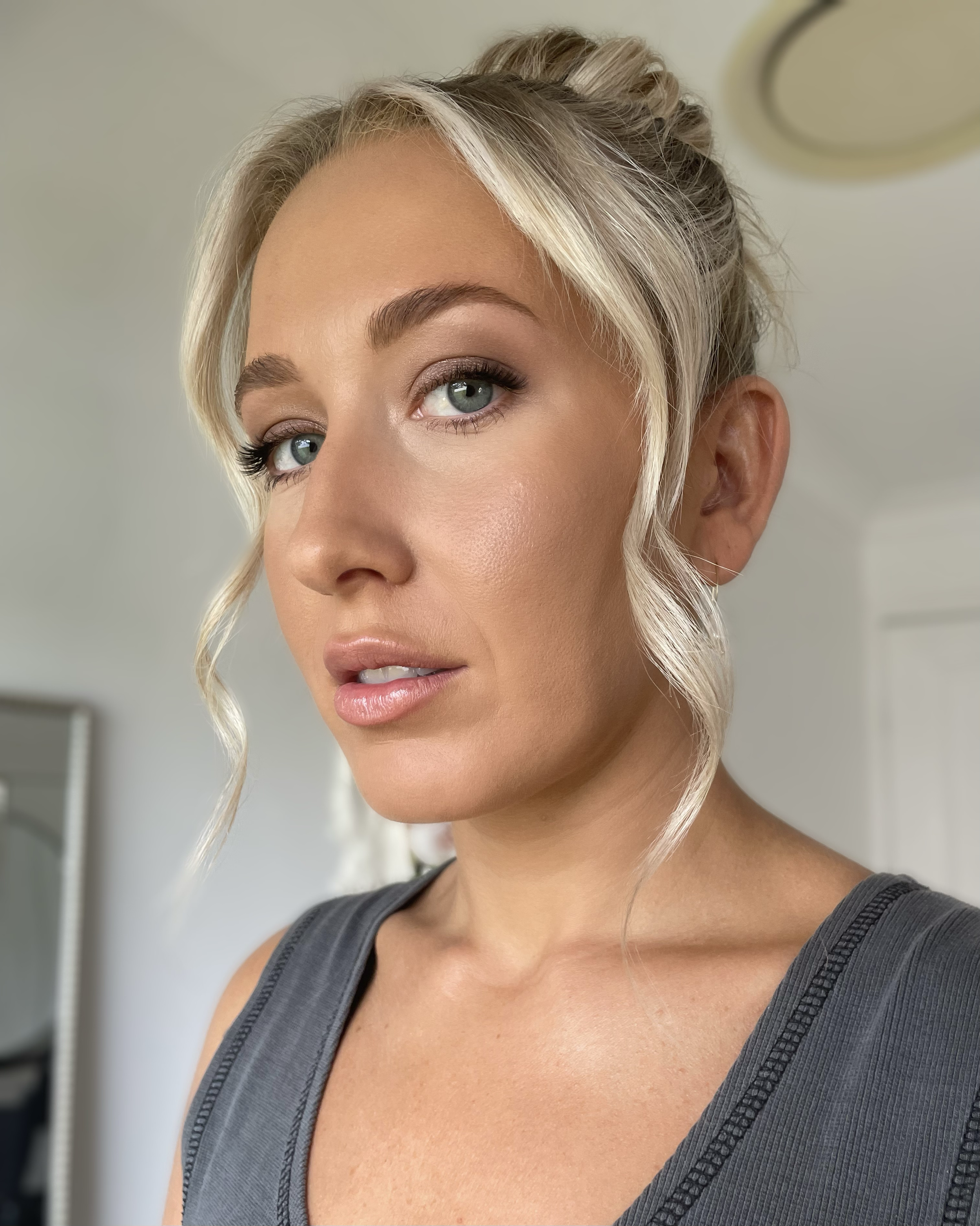 Close-up of a woman with blonde hair and blue eyes, styled in an updo, wearing a grey sleeveless top.