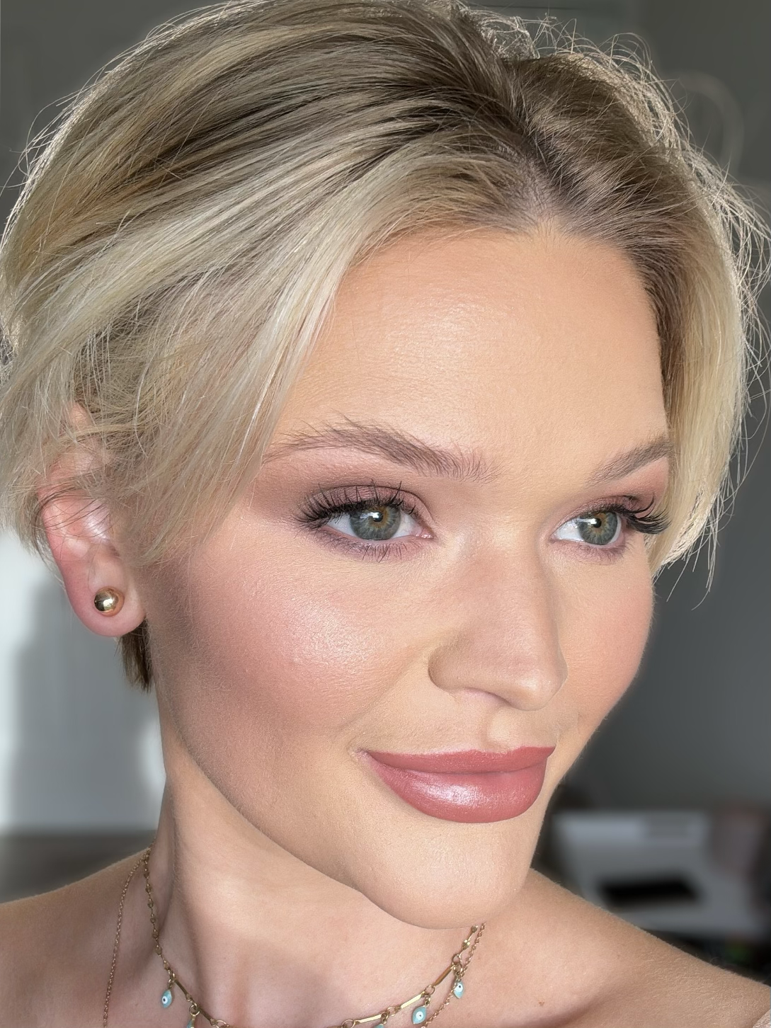 Woman with short blonde hair, wearing makeup and jewelry, smiling slightly.
