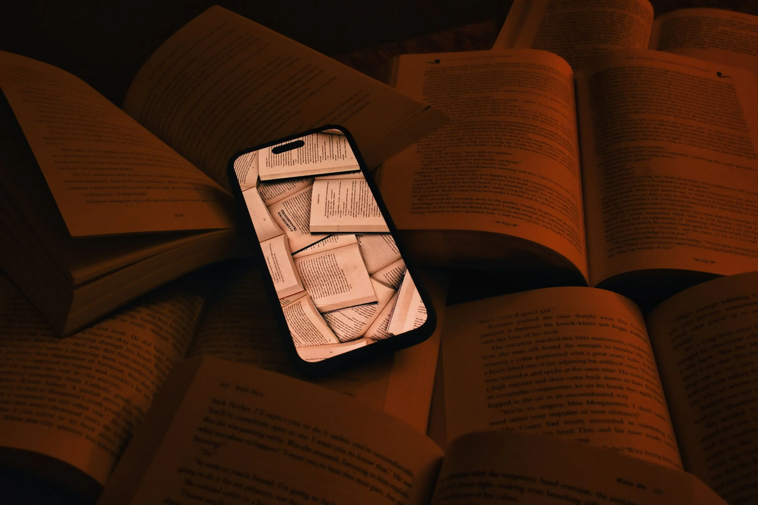 Smartphone displaying stacked book pages surrounded by open books, illustrating the relationship between print, digital media, reading, artificial intelligence, and the evolution of storytelling.