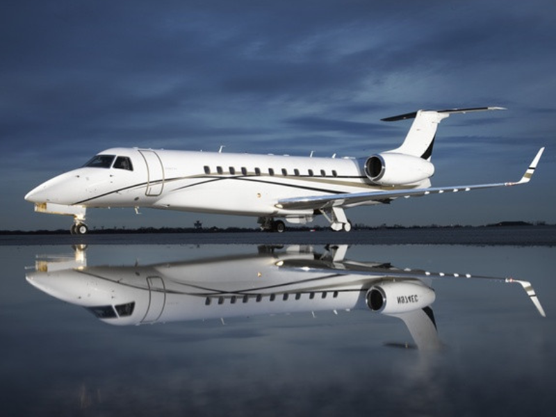 Private jet on a tarmac with reflection in wet ground, under a cloudy sky.