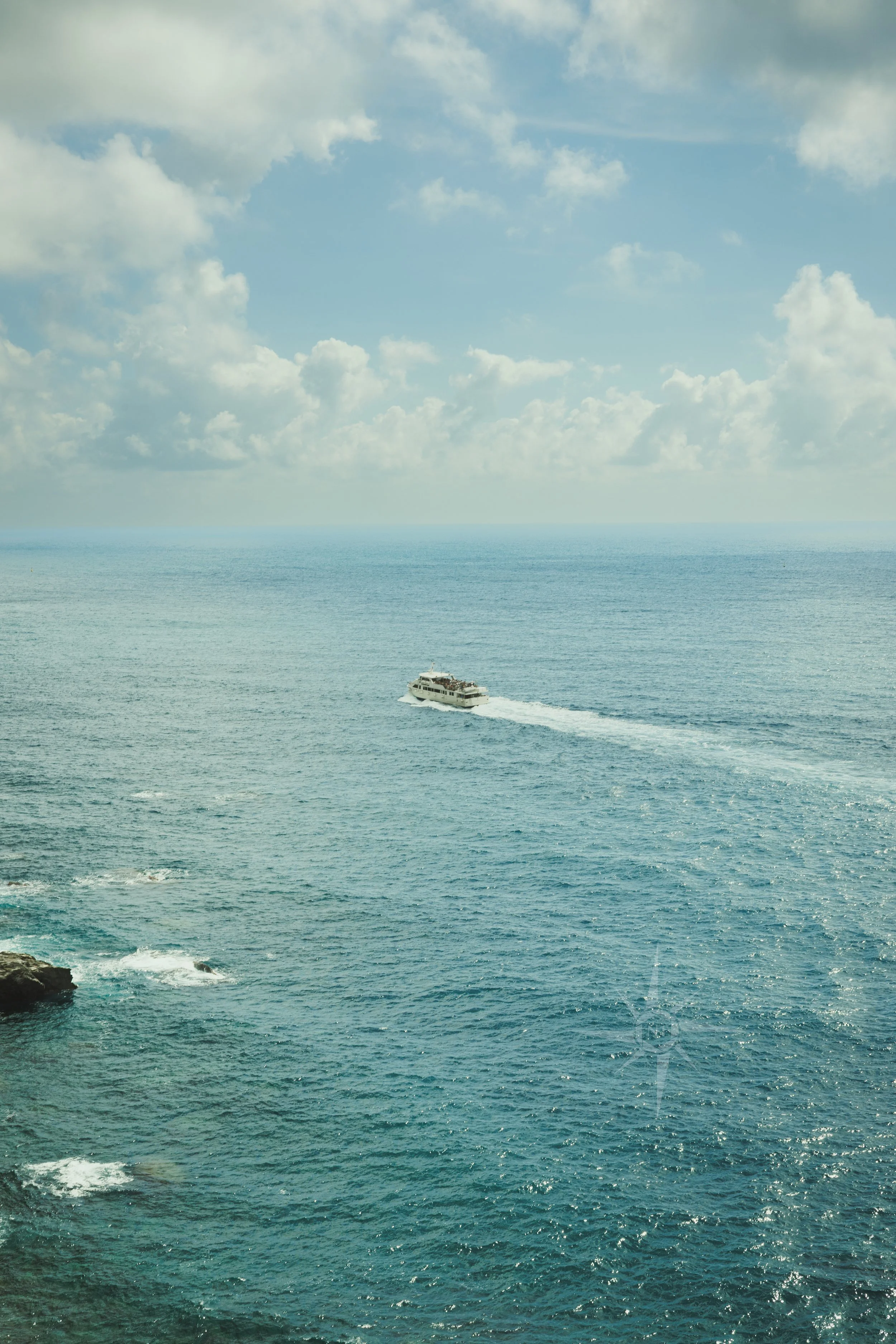 A boat sailing on the ocean with a blue sky overhead filled with clouds.