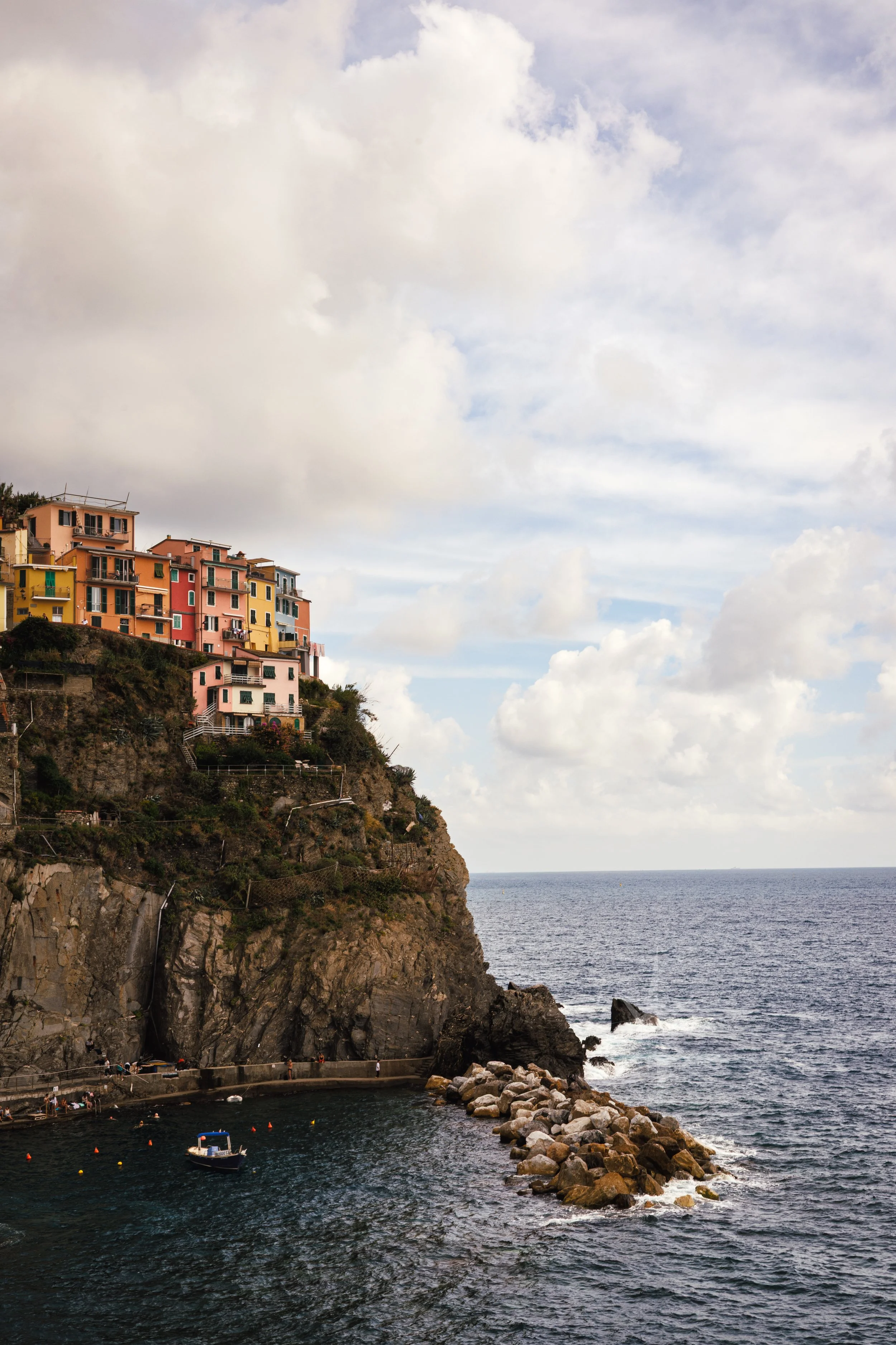 Colorful buildings on a cliff overlooking the ocean with a small harbor.