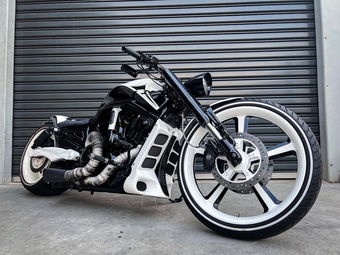 Custom black and white motorcycle with large front wheel and white accents, parked in front of a gray metal garage door.