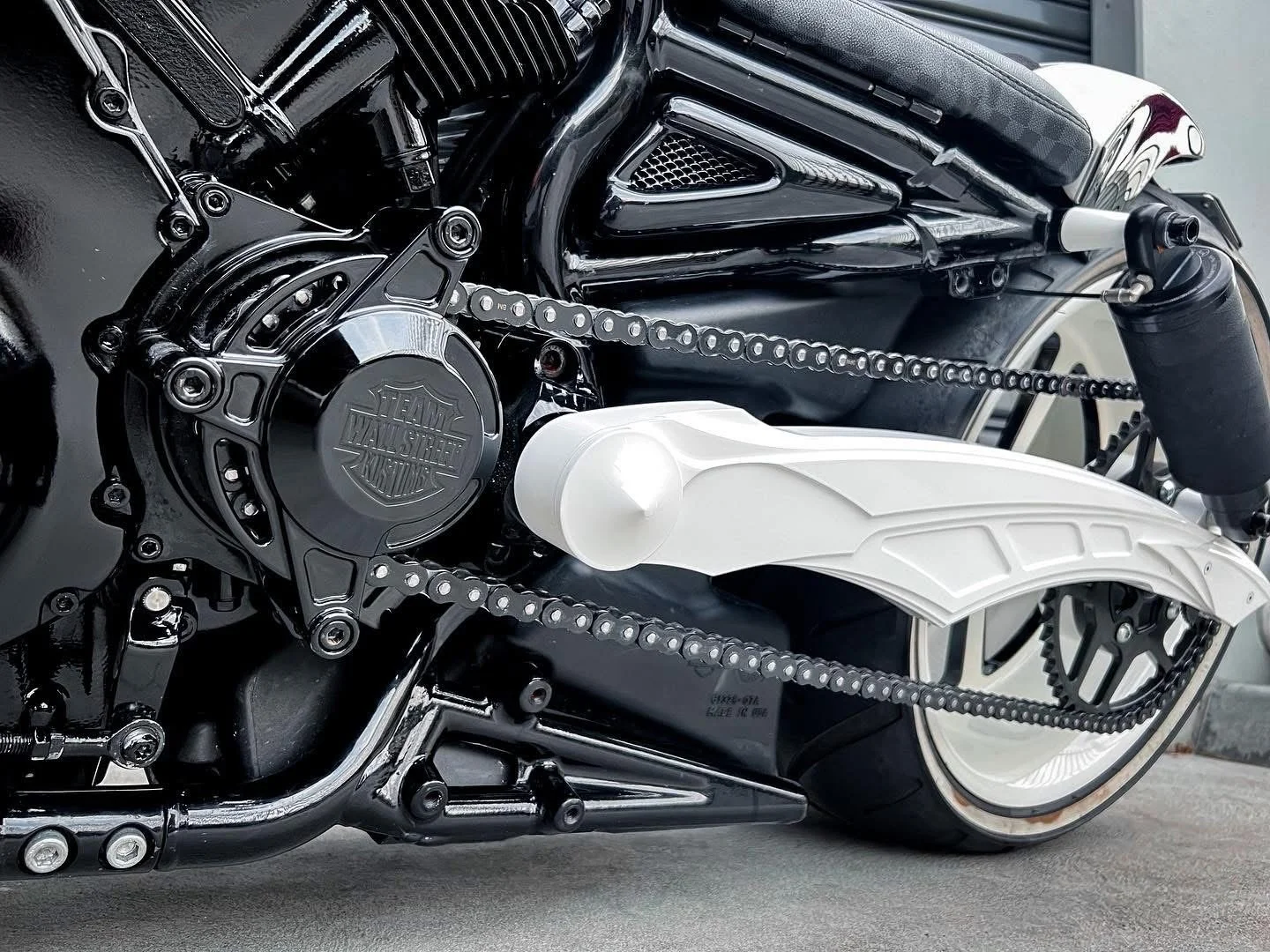 Close-up of a black Harley-Davidson motorcycle's engine and chain, with a white rear fender and black tire.