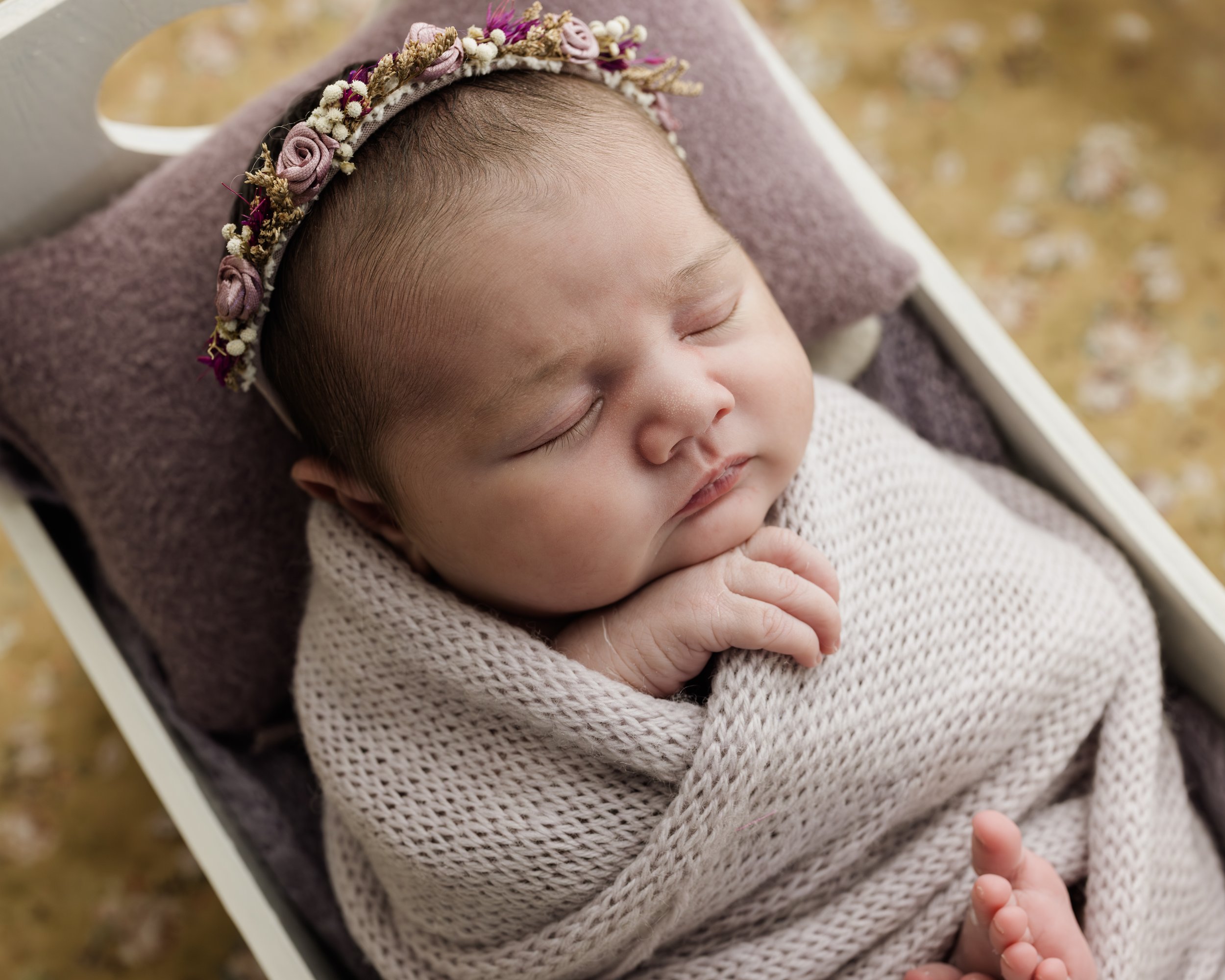 A newborn baby in a studio setting, photographed with a flower tieback and dressed in hand-knitted wraps by photographer Georgia Politis