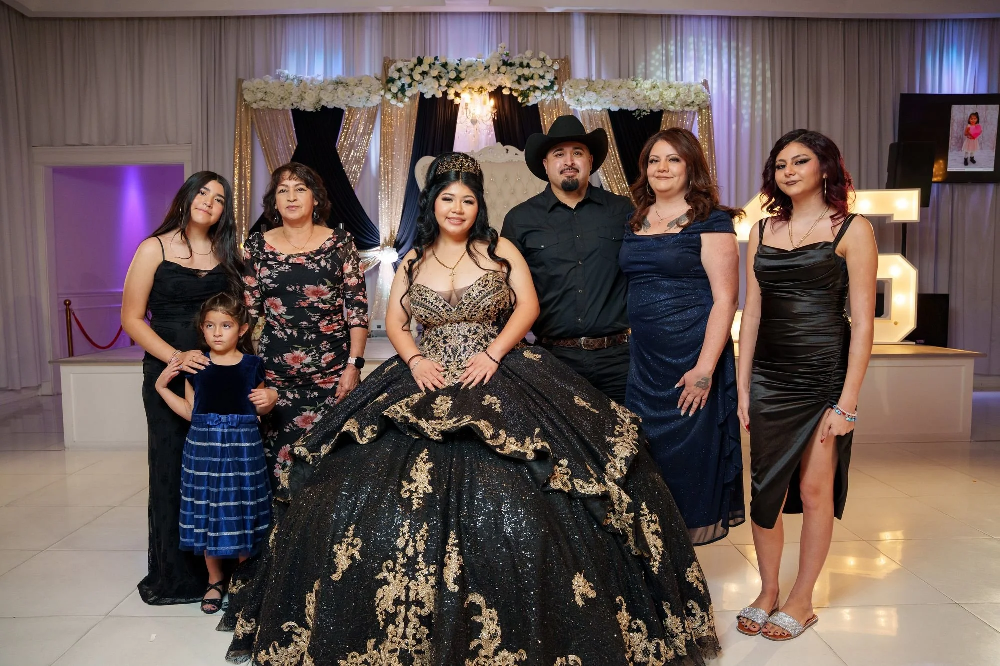 Jayden with her parents, grandmother, and flower girl in coordinated black and gold attire posing for formal family portrait at her quinceañera at Luxor Banquet Hall Carrollton