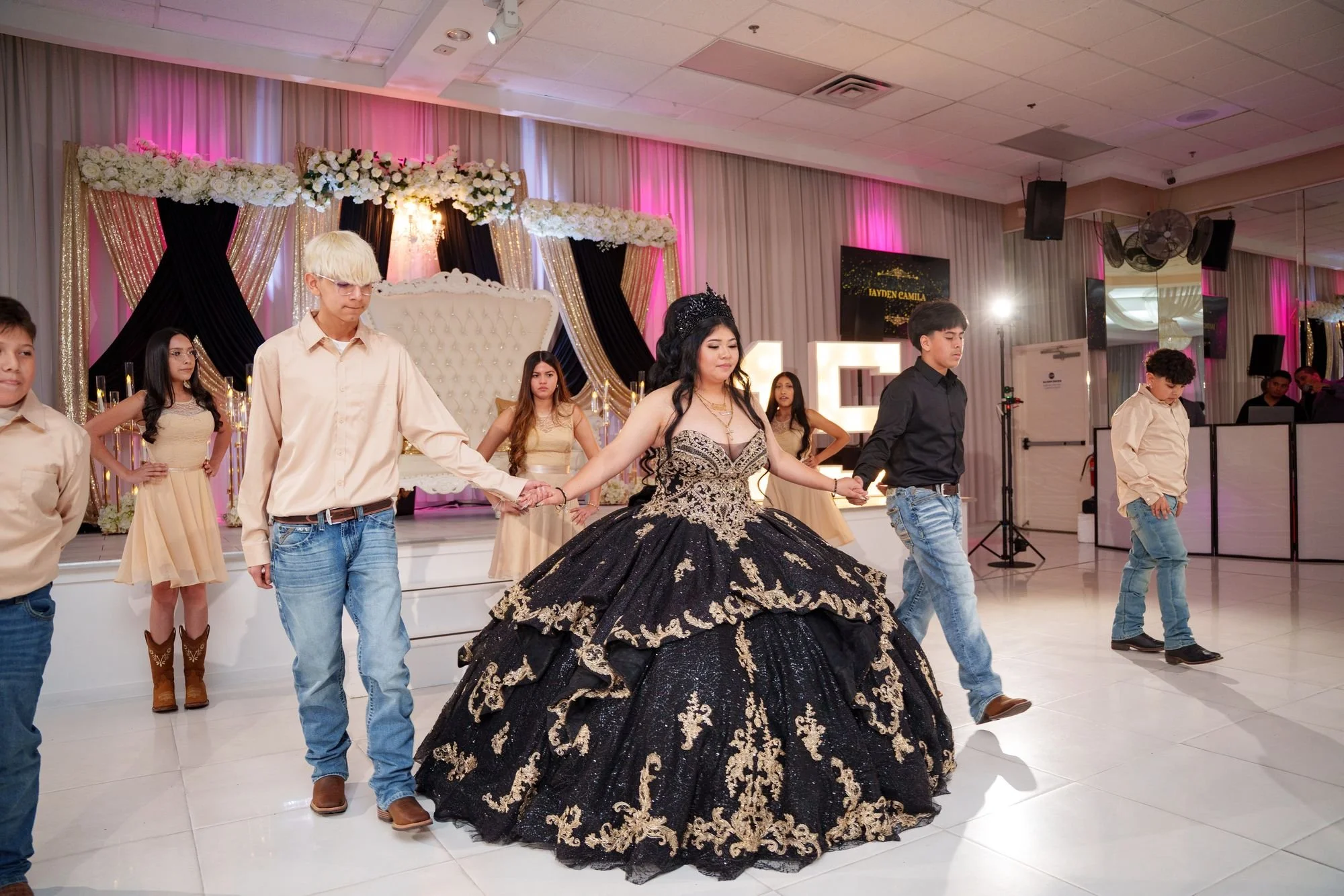 Jayden in the center of her quinceañera court holding hands in a synchronized line formation with damas and chambelanes during the opening dance at Luxor Banquet Hall Carrollton