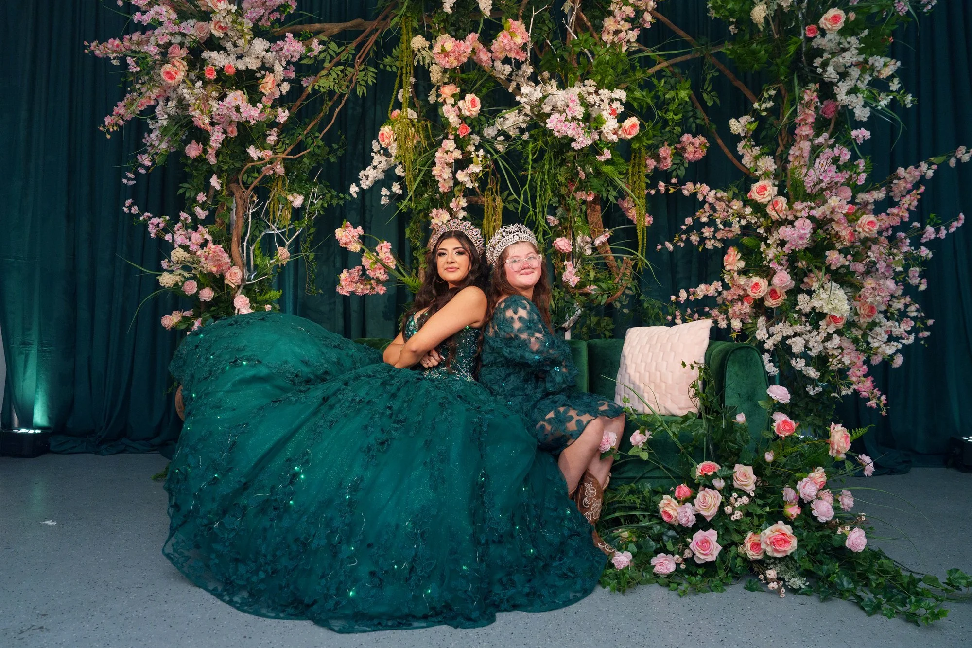 Nevaeh posing with her emerald green quinceañera ballgown train fanned out dramatically in front of a pink floral wall