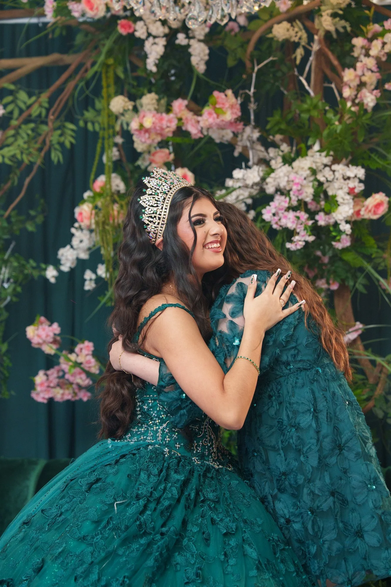 Nevaeh embracing her younger sister in front of the illuminated NEVAEH marquee letters, both crowned and in emerald