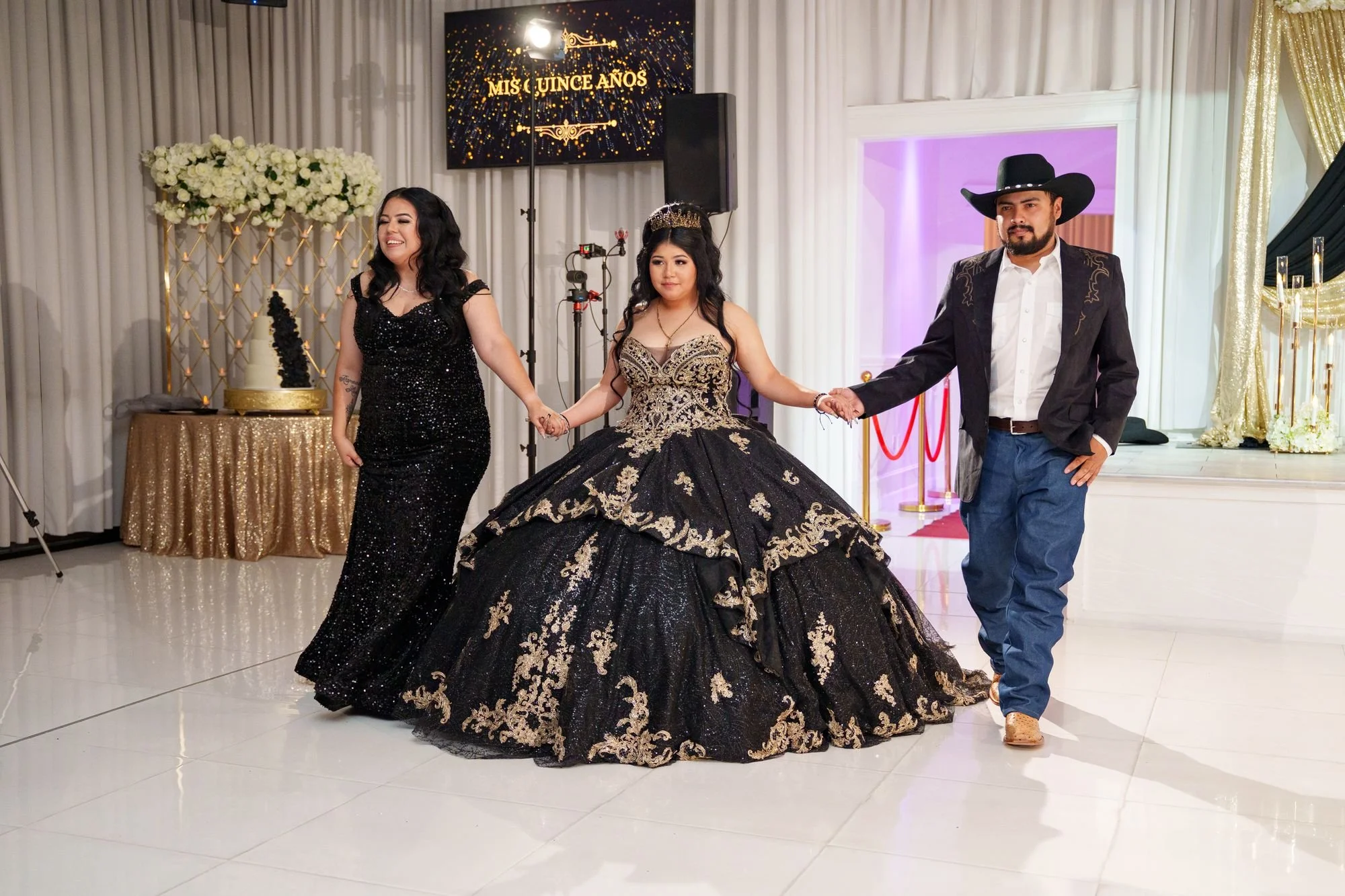 Jayden walking onto the dance floor flanked by her mother in black sequin gown and father in cowboy hat for grand entrance at her quinceañera at Luxor Banquet Hall Carrollton