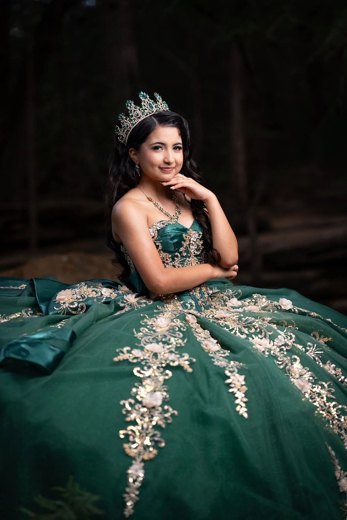  Close portrait of quinceañera in emerald gown with gold embroidery and emerald crystal crown, enchanted forest setting at Stone Creek Park, Flower Mound TX 