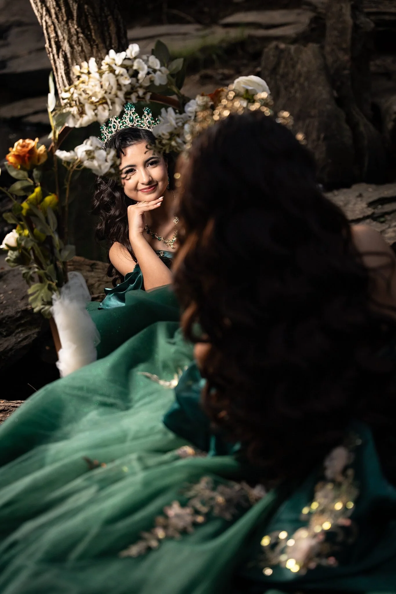  Quinceañera posing beside white and orange floral arch in a mirror reflection setup, enchanted forest theme at Stone Creek Park in Flower Mound, TX 