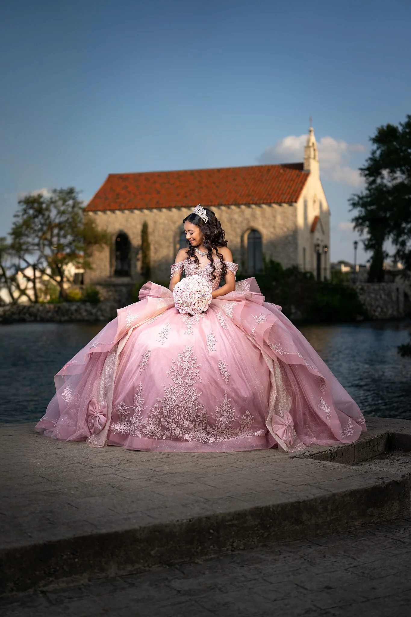 Quinceañera con vestido de gala rosa sosteniendo su ramo frente a la capilla Bella Donna en Adriatica Village, McKinney, TX