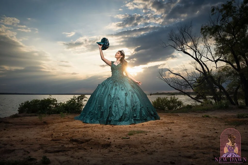  Quinceañera in emerald gown holding bouquet raised triumphantly at sunset over Lake Grapevine in Flower Mound, TX 