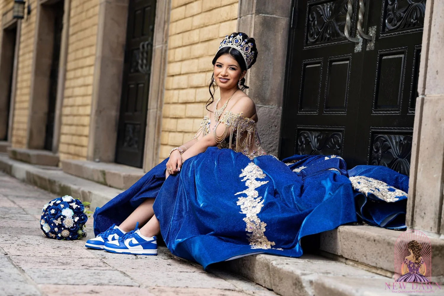 Quinceañera con vestido azul rey y tenis Nike Dunk azules personalizados, sentada en escalones de piedra mediterráneos en Las Colinas, Irving, TX