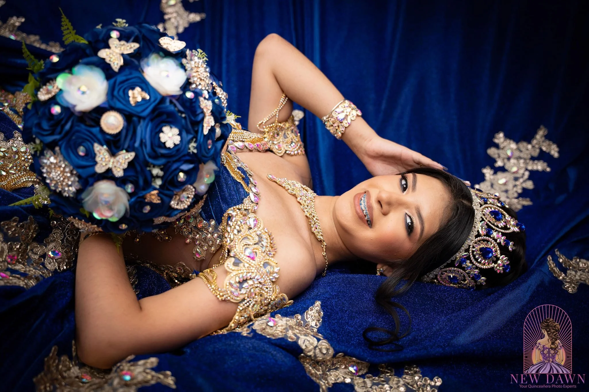  Overhead portrait of quinceañera in royal blue gown with gold beadwork and a blue rose brooch bouquet at Mandalay Canal Walk in Las Colinas 