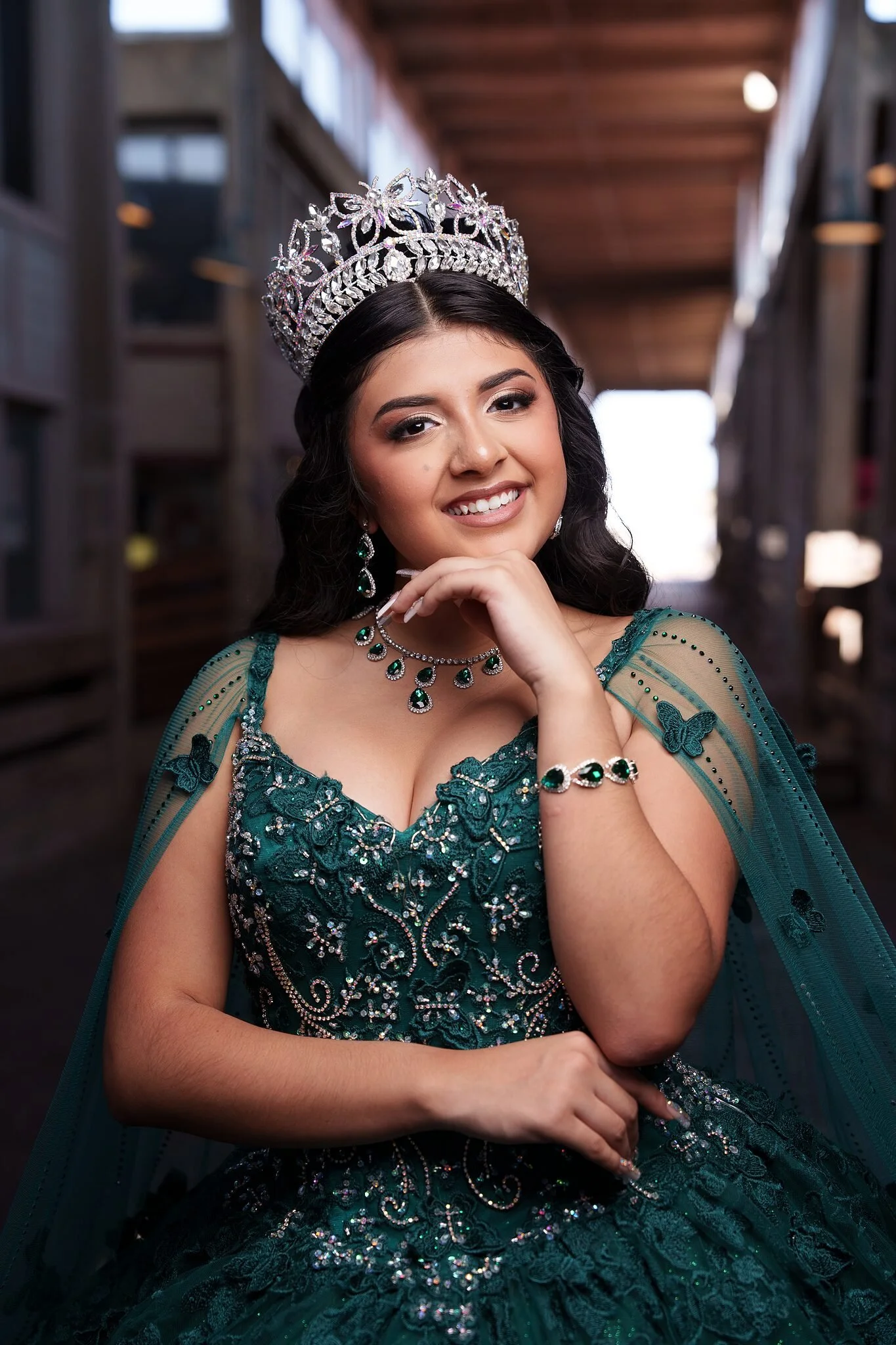 Retrato de quinceañera con vestido verde esmeralda y corona de cristal en el corredor histórico de madera del Fort Worth Stockyards