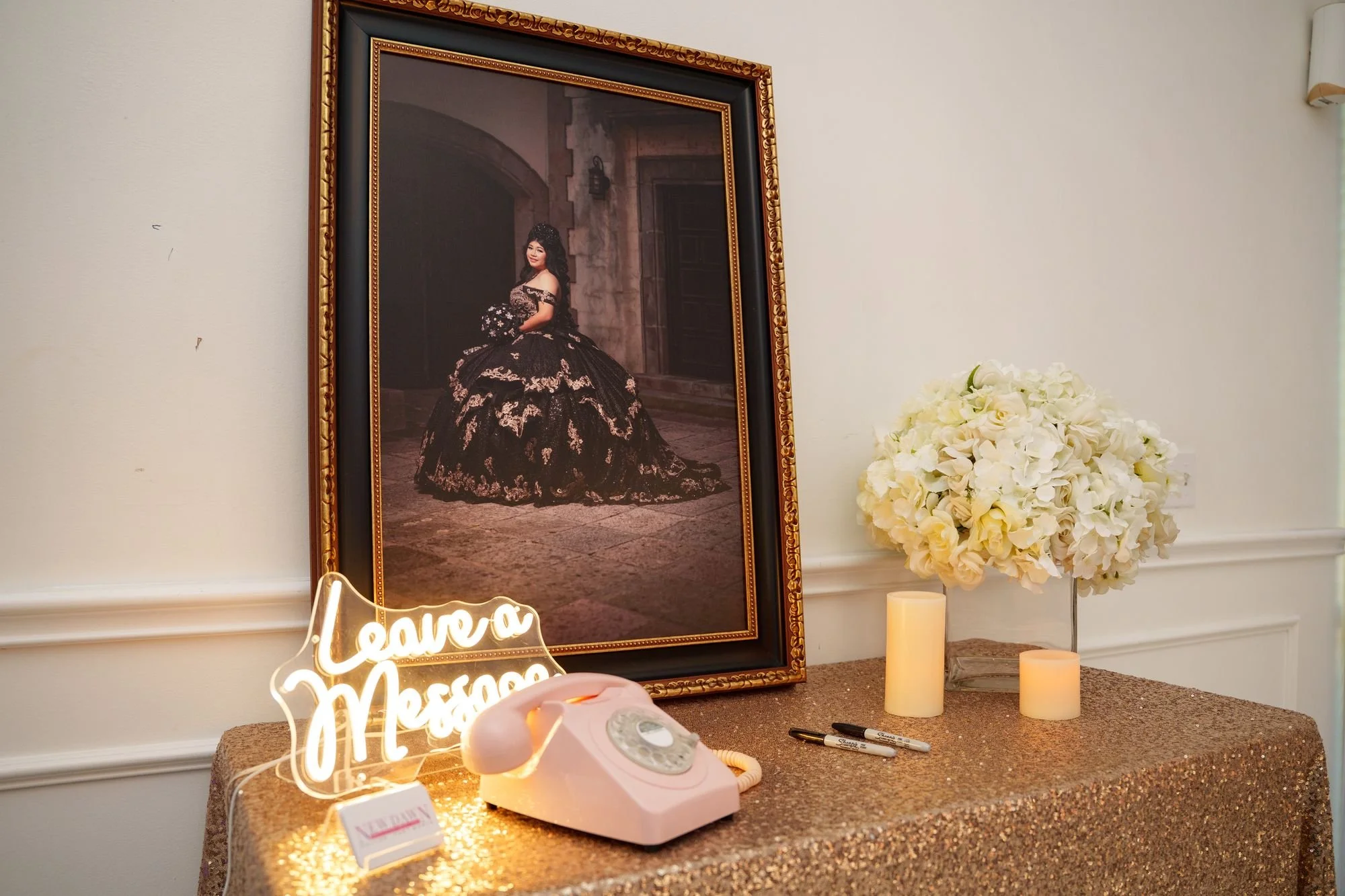 Phone Audio Guestbook station with vintage rotary phone, framed Jayden portrait, white floral arrangement, candles, and sunset lighting on gold sequin tabletop at Luxor Banquet Hall Carrollton quinceañera