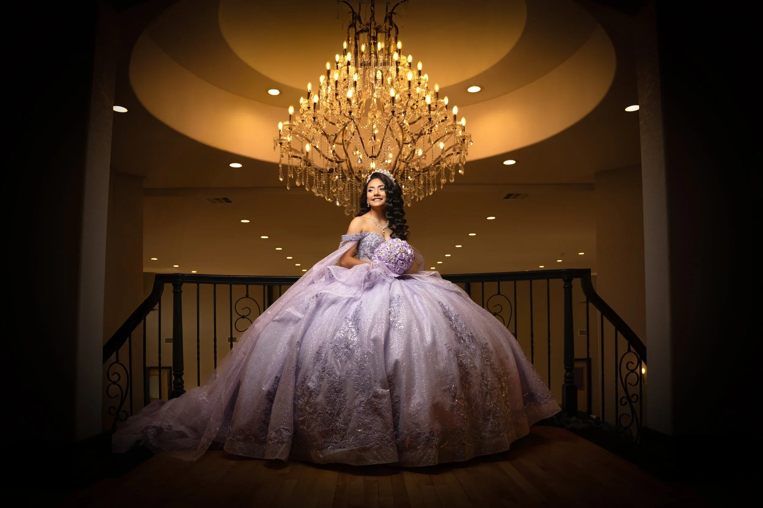 Quinceañera in a lavender ballgown posing beneath a grand crystal chandelier for a formal portrait in Dallas–Fort Worth