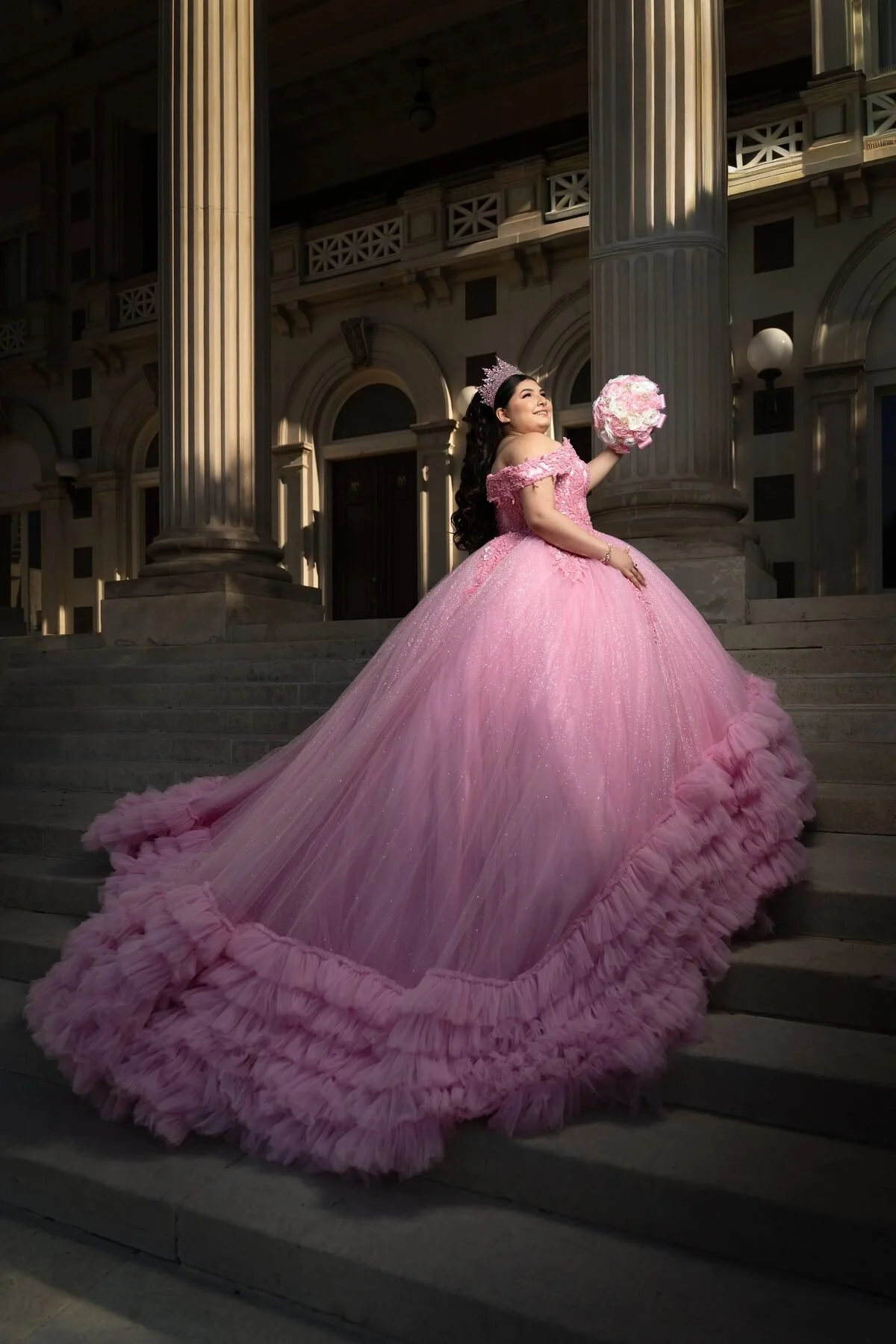 Quinceañera in a pink ball gown with a long train by columns at night in Texas