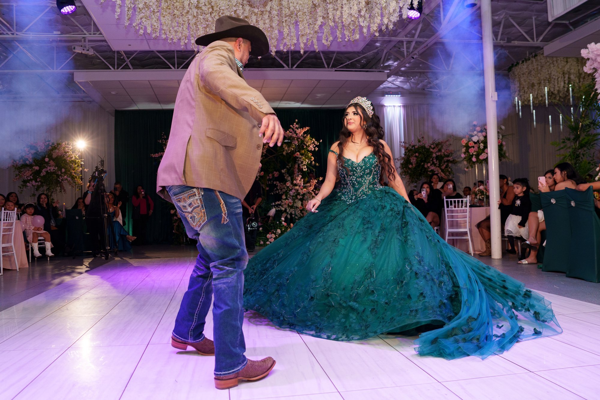 Father-daughter dance at Nevaeh's quinceañera, father wearing a cowboy hat, dance floor enveloped in theatrical fog with chandeliers above